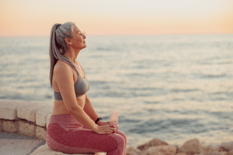 Close-up photo of sporty female sitting on the edge of shore with her eyes closed, relaxing