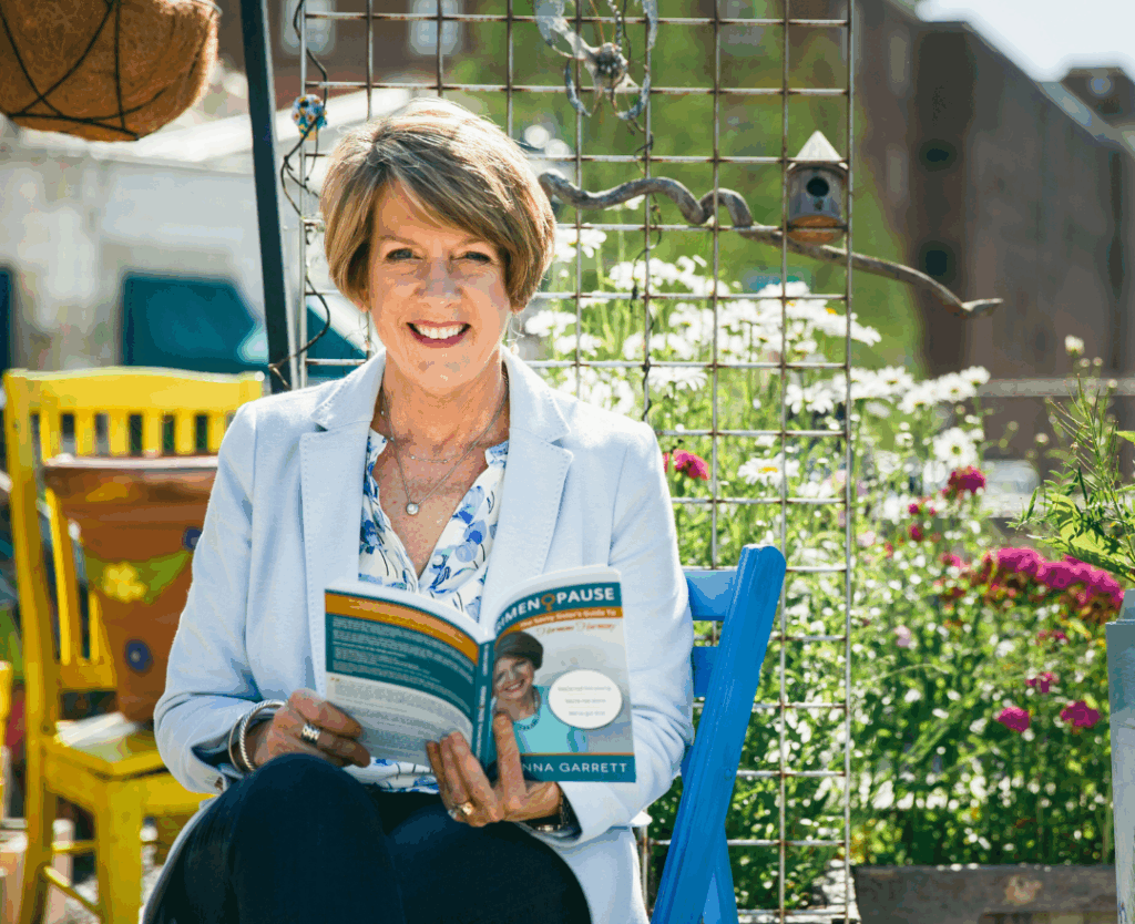 Dr. Anna Garrett, hormone specialist, smiling while holding her Menopause book in a garden setting wearing a light blue blazer