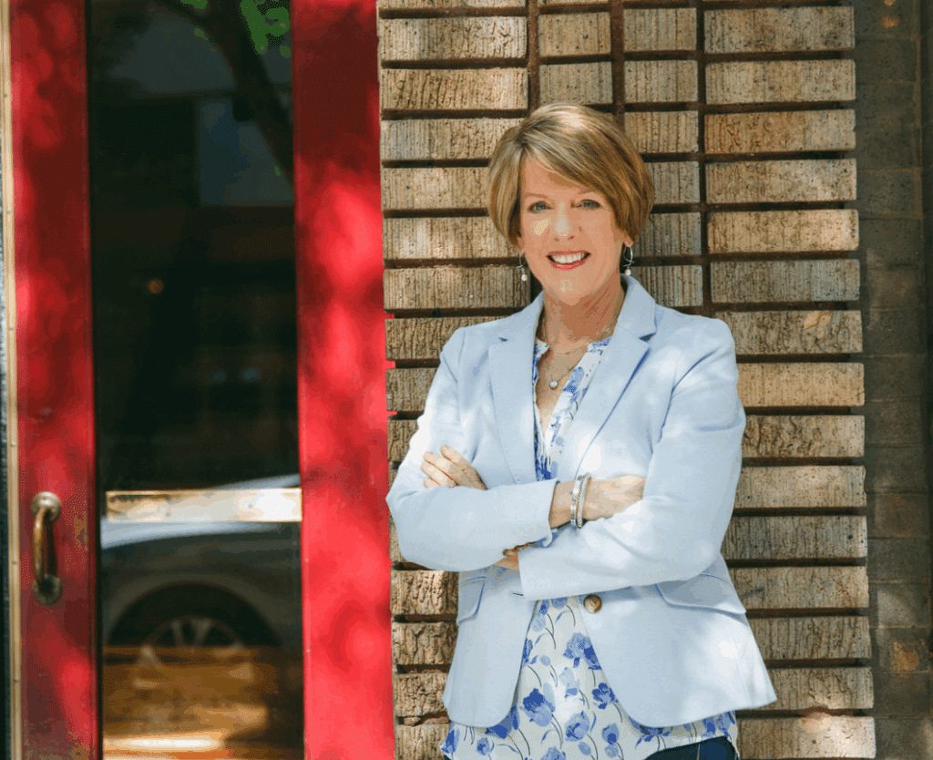 Dr. Anna Garrett, menopause and hormone expert, standing confidently with arms crossed in light blue blazer and floral dress outside brick building
