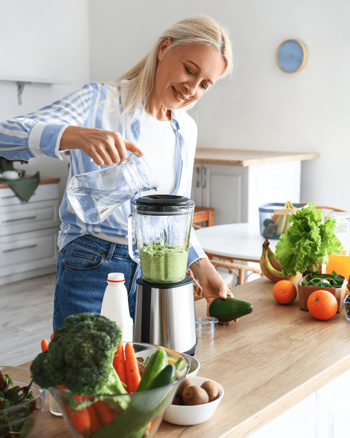 Mature woman making healthy smoothie with blender in kitchen