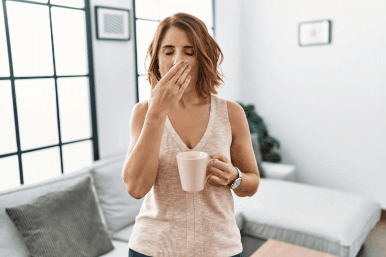 Middle age woman drinking a cup coffee at home bored yawning tired covering mouth with hand. Tired and sleepy.