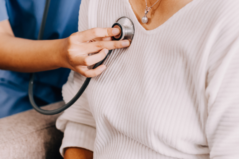 Healthcare provider using stethoscope to check heart health of midlife woman in white sweater during cardiovascular screening