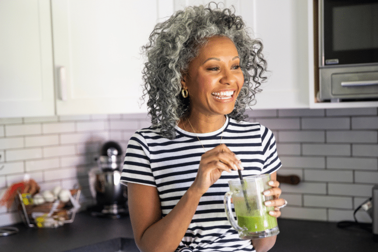 Midlife woman drinking a green smoothie in her kitchen to support gut health and bone loss prevention