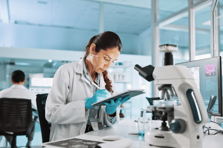 Female researcher in lab coat reviewing peptide research data on a tablet beside a microscope, representing FDA peptide compounding review.