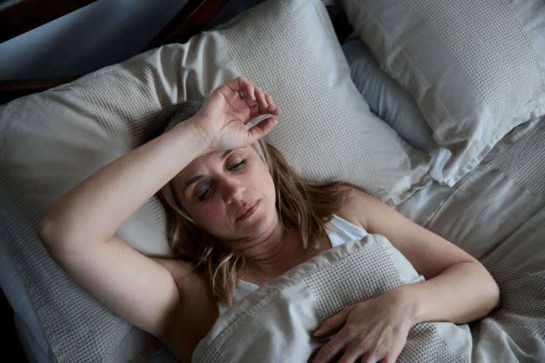 Midlife woman lying awake in bed with hand on forehead, showing signs of insomnia linked to hormone and gut health changes