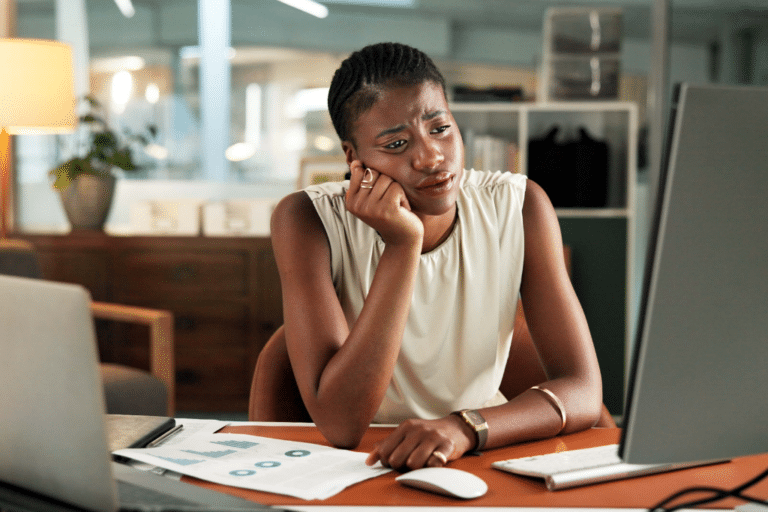 Woman with perimenopause brain fog resting her head on her hand, looking tired and frustrated while working at her computer