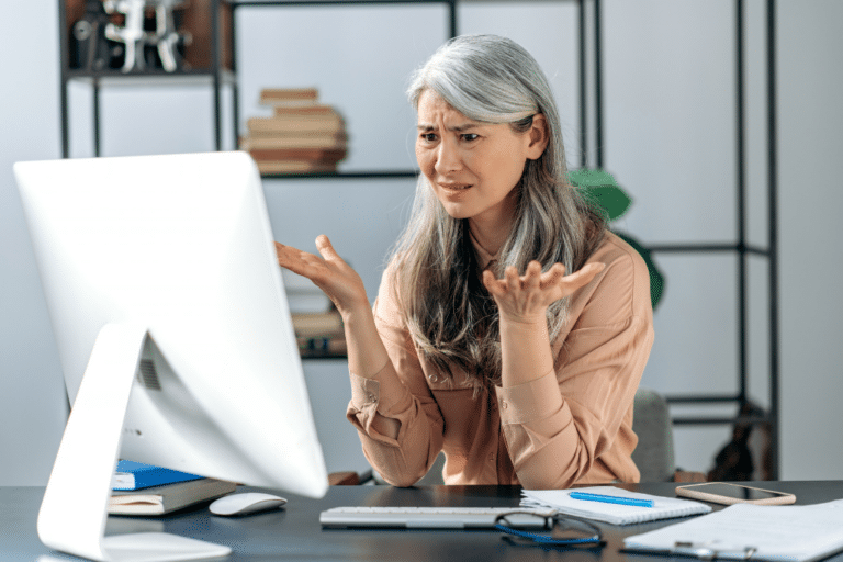 Confused midlife woman with long gray hair gesturing at her computer screen, wondering how much estrogen is enough in menopause